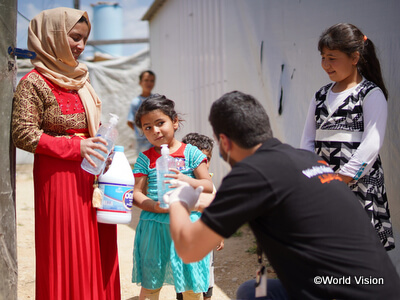 （画像：シリア難民の人々に漂白剤や除菌用品を配布する様子）